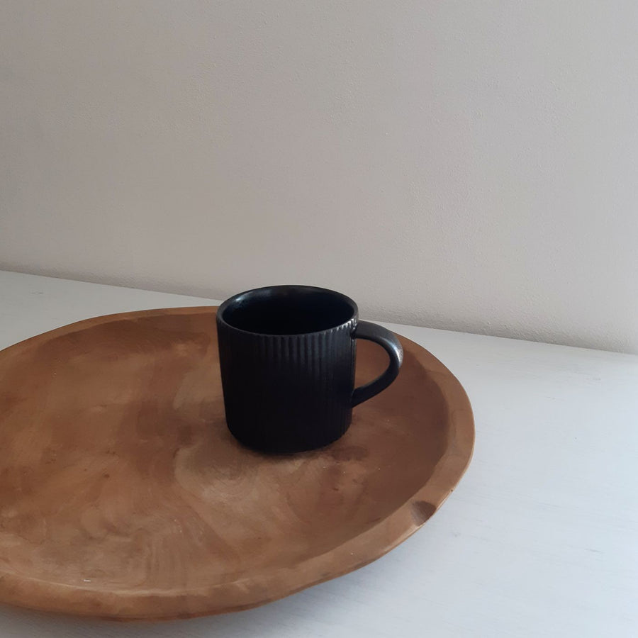 A simple undecorated ceramic mug, photographed resting on a round wooden plate.