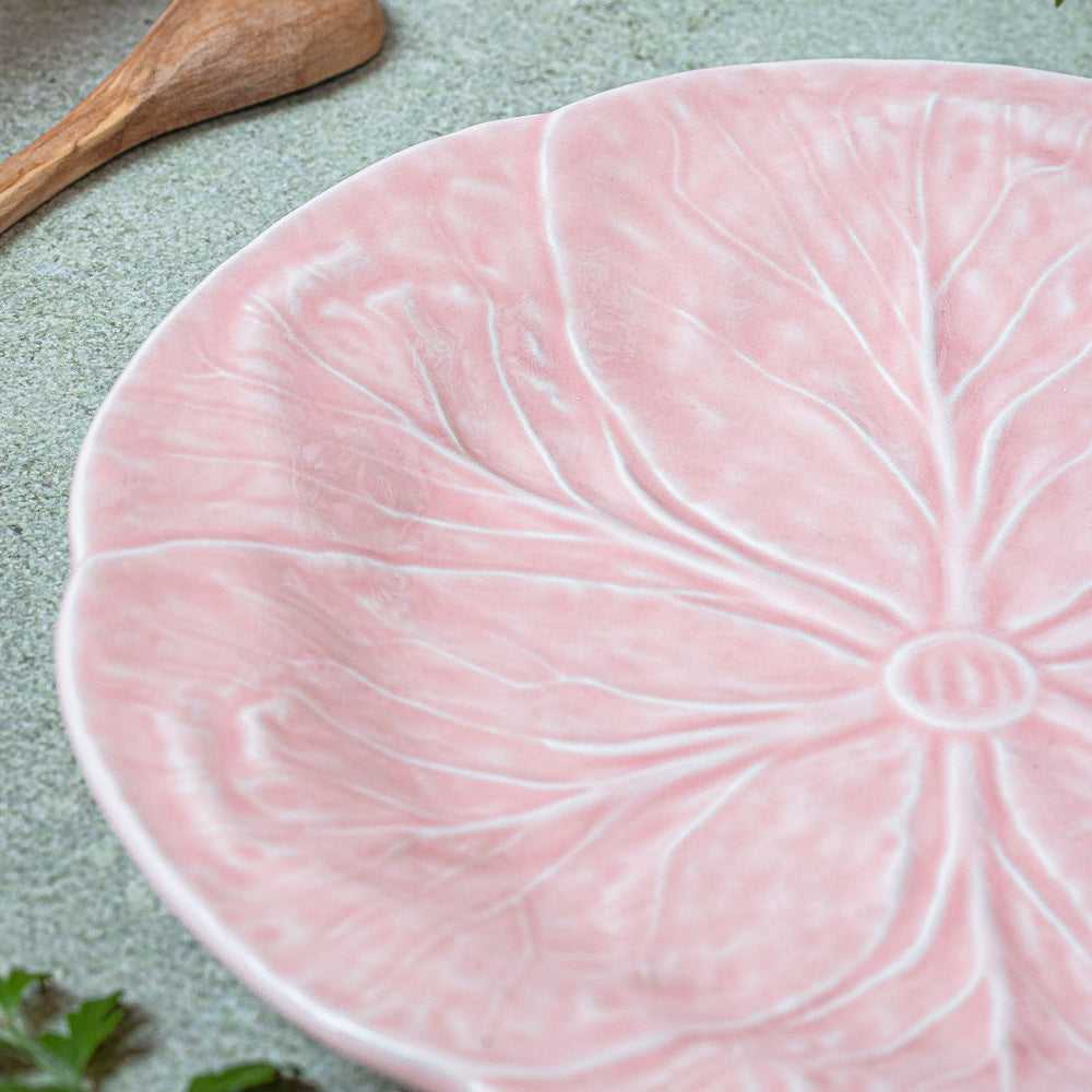 An elegant pink ceramic plate carrying a leaf pattern, shown close up on a textured surface.