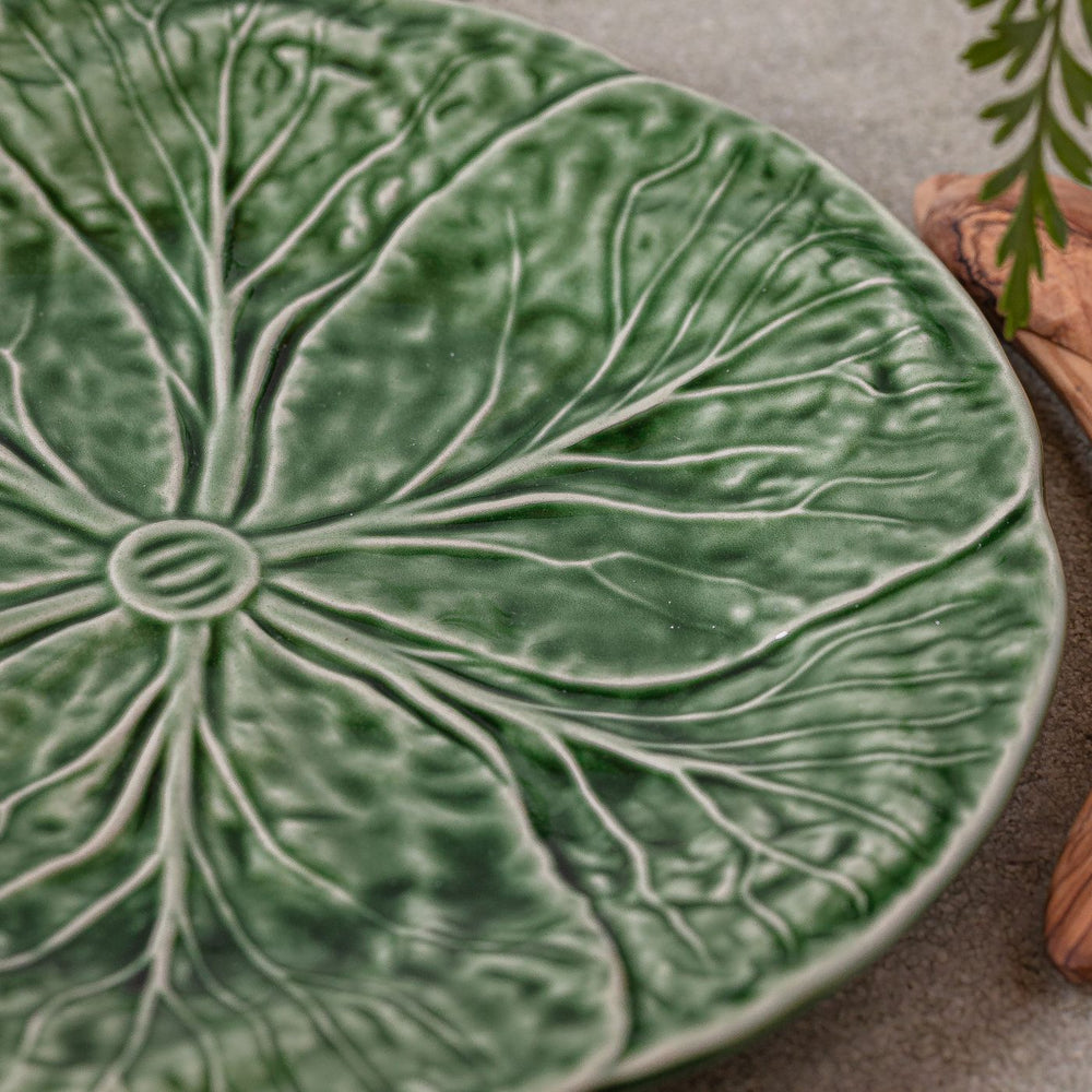 An artistic ceramic plate with a green leaf pattern running across the face.