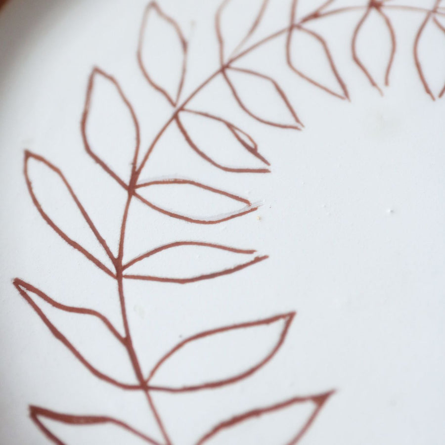 A beige ceramic plate with an artistic brown leaf pattern brushed across it.