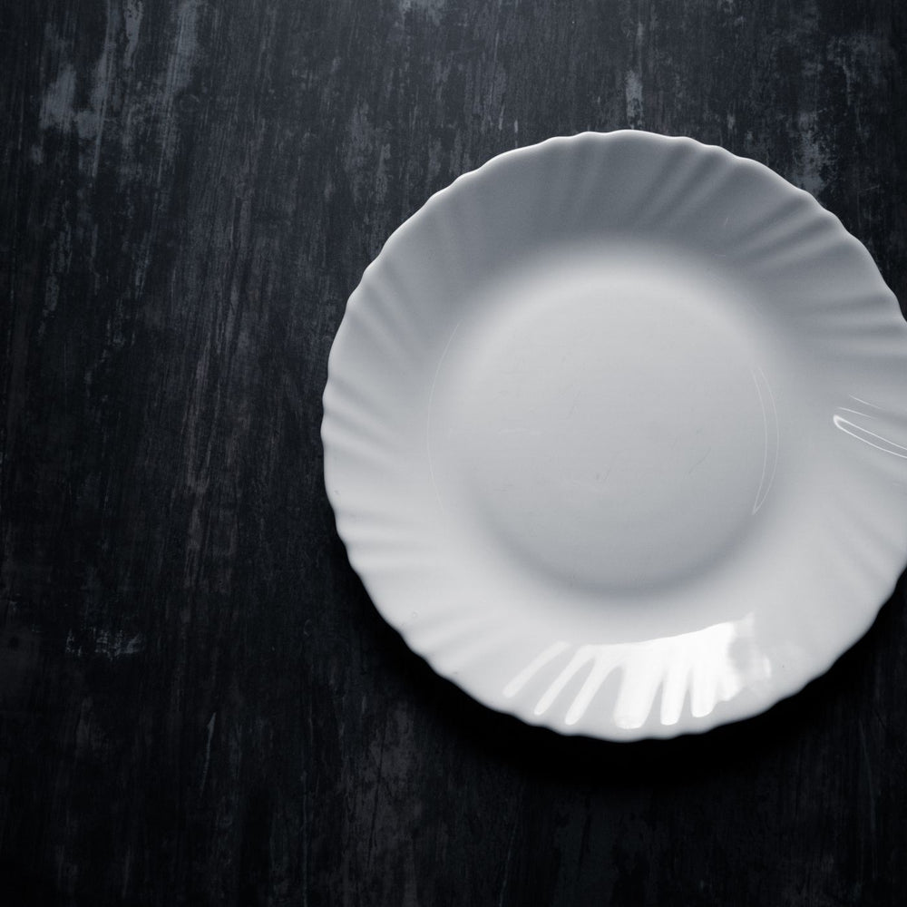 A clean white ceramic plate, photographed from above on a dark textured background.