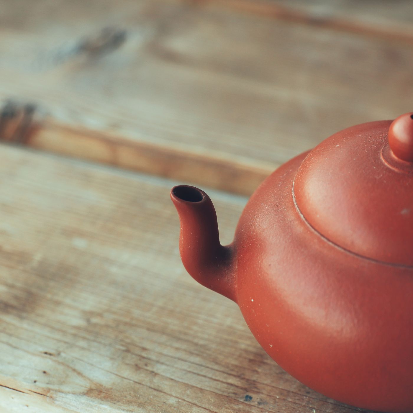 A red clay teapot, photographed in soft light on a rustic wooden table.