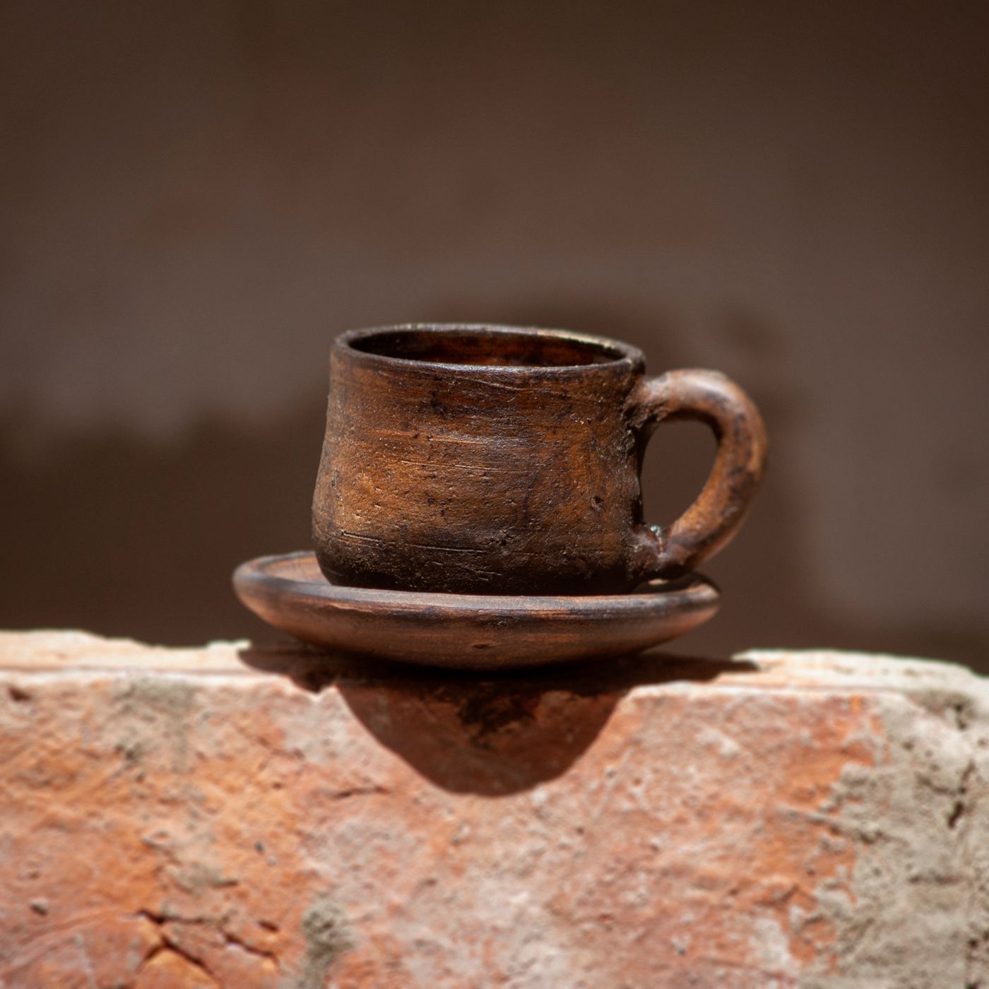 A classic clay coffee cup with its matching saucer, shown against a warm earthy backdrop.