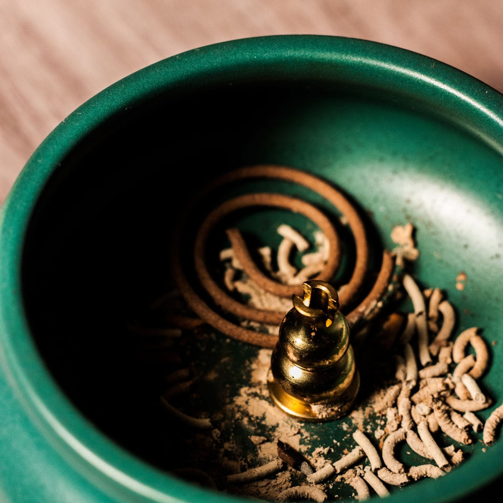 A green ceramic holder made for coiled incense, shown holding a coil on its brass coil support.
