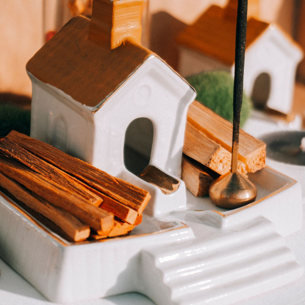 A ceramic incense holder shaped like a small house, shown in a still life with palo santo sticks.
