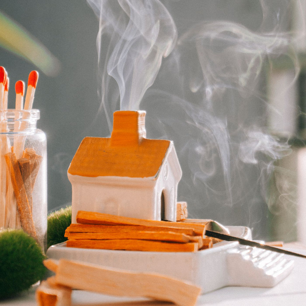 A miniature ceramic house incense burner, photographed indoors with gentle smoke rising from it.
