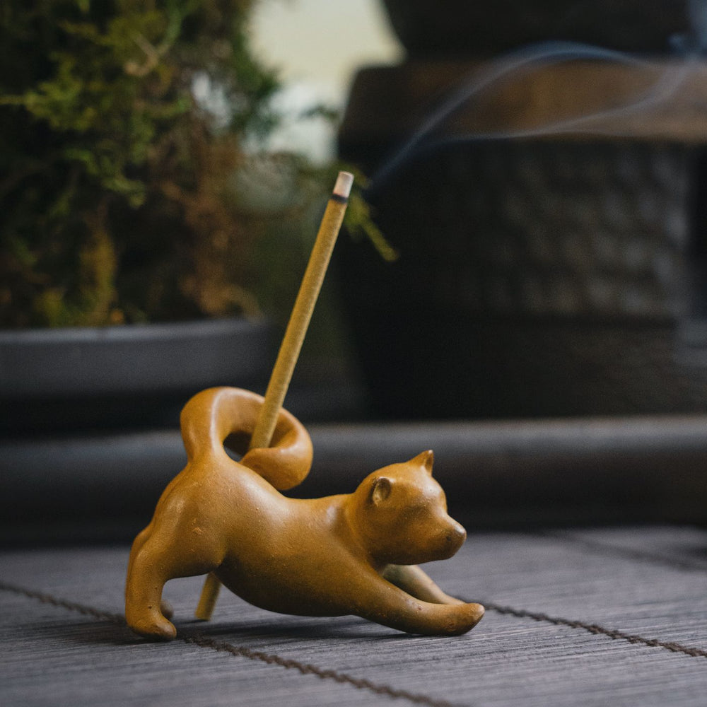 A small ceramic cat figurine that works as an incense holder, photographed outdoors on a table with smoke rising.