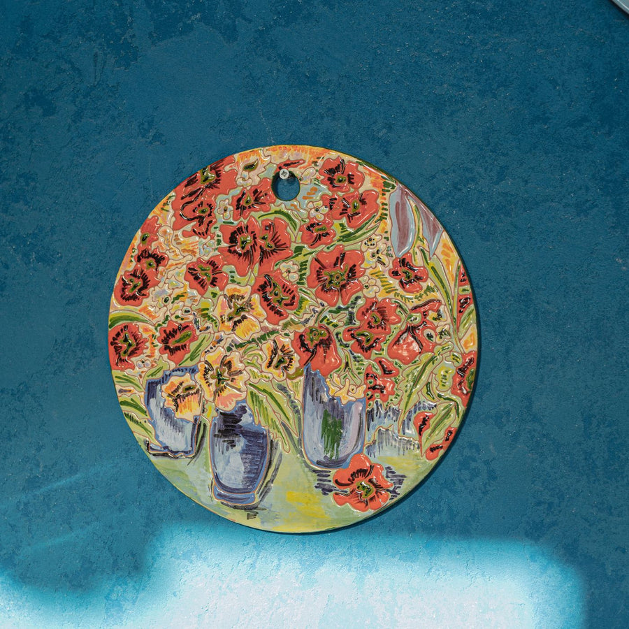 An artistic handmade plate with a vibrant floral design, shown against a blue background.