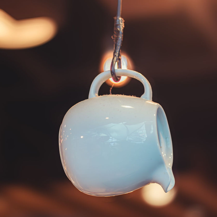 A white ceramic pitcher, photographed indoors suspended artistically on a wire.