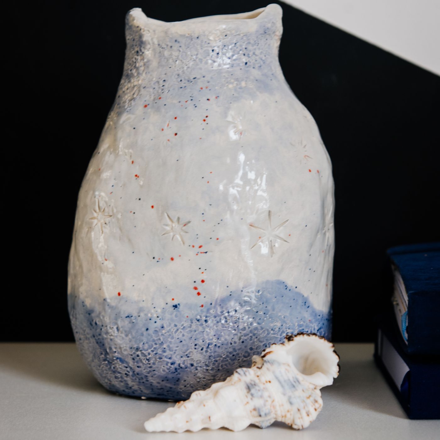 A handmade pottery vase with an ocean inspired design, finished with a decorative seashell on the body.