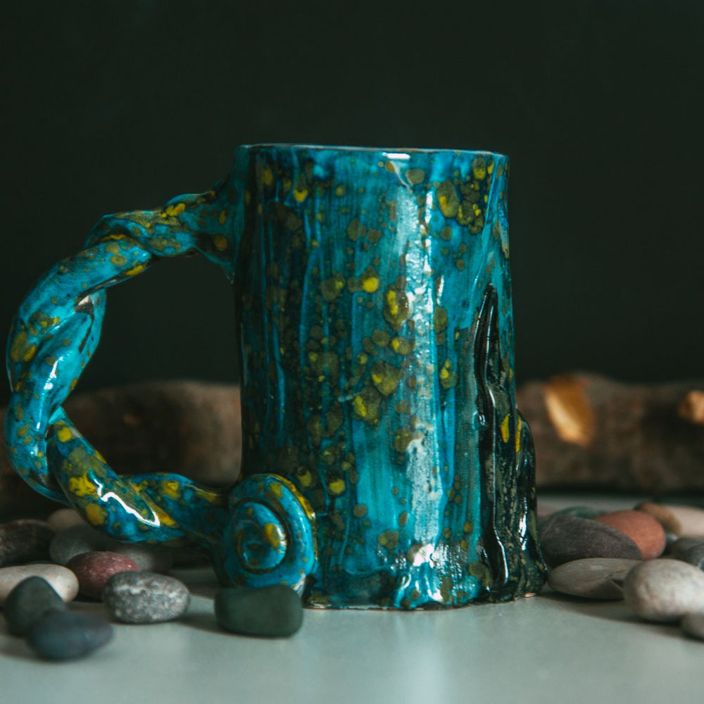 A quirky blue handmade mug, shown close up among a scatter of pebbles.