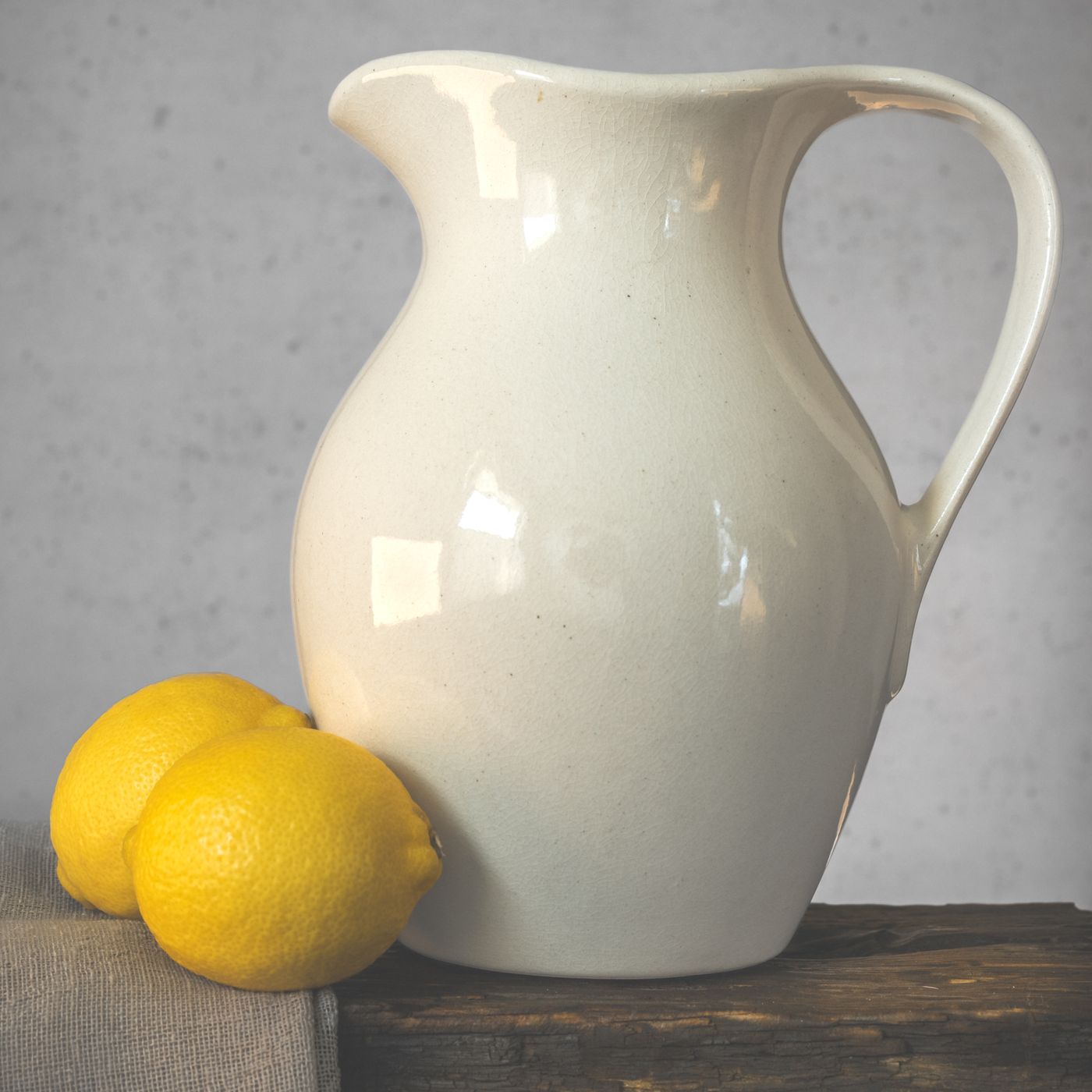 A porcelain jug photographed as a still life on a rustic table beside a few lemons.