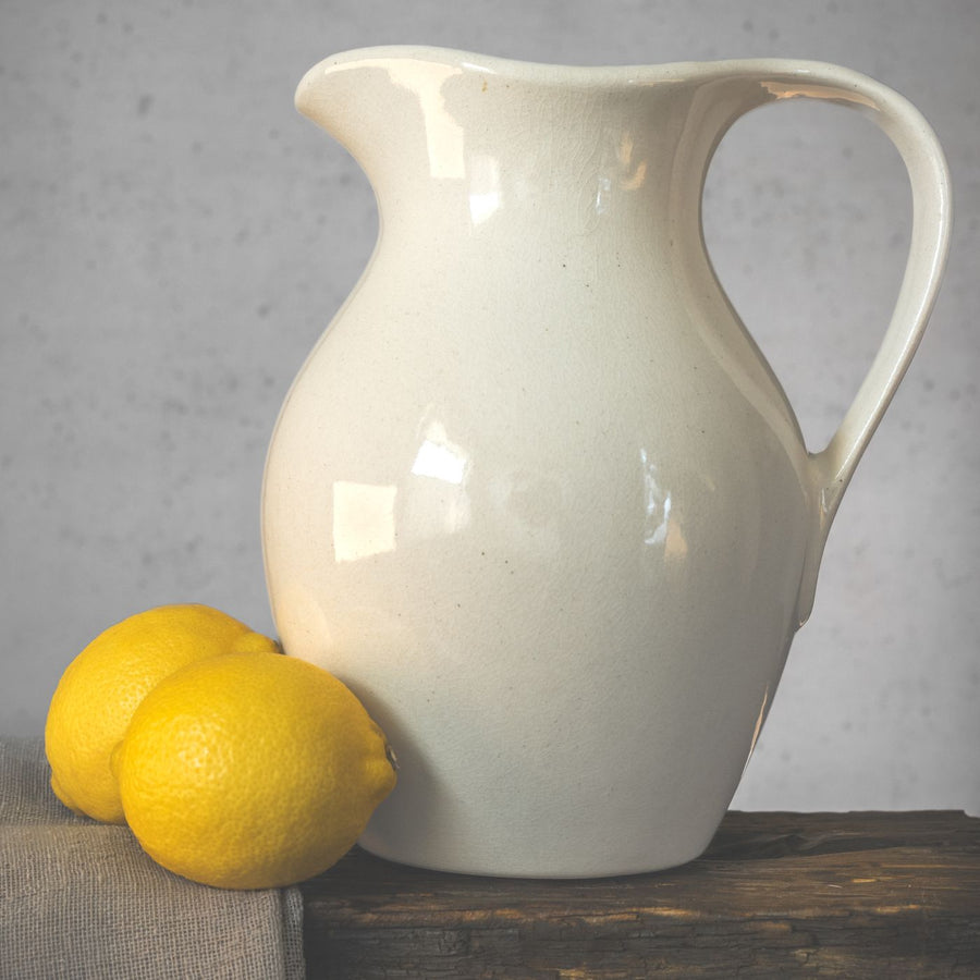 A porcelain jug photographed as a still life on a rustic table beside a few lemons.