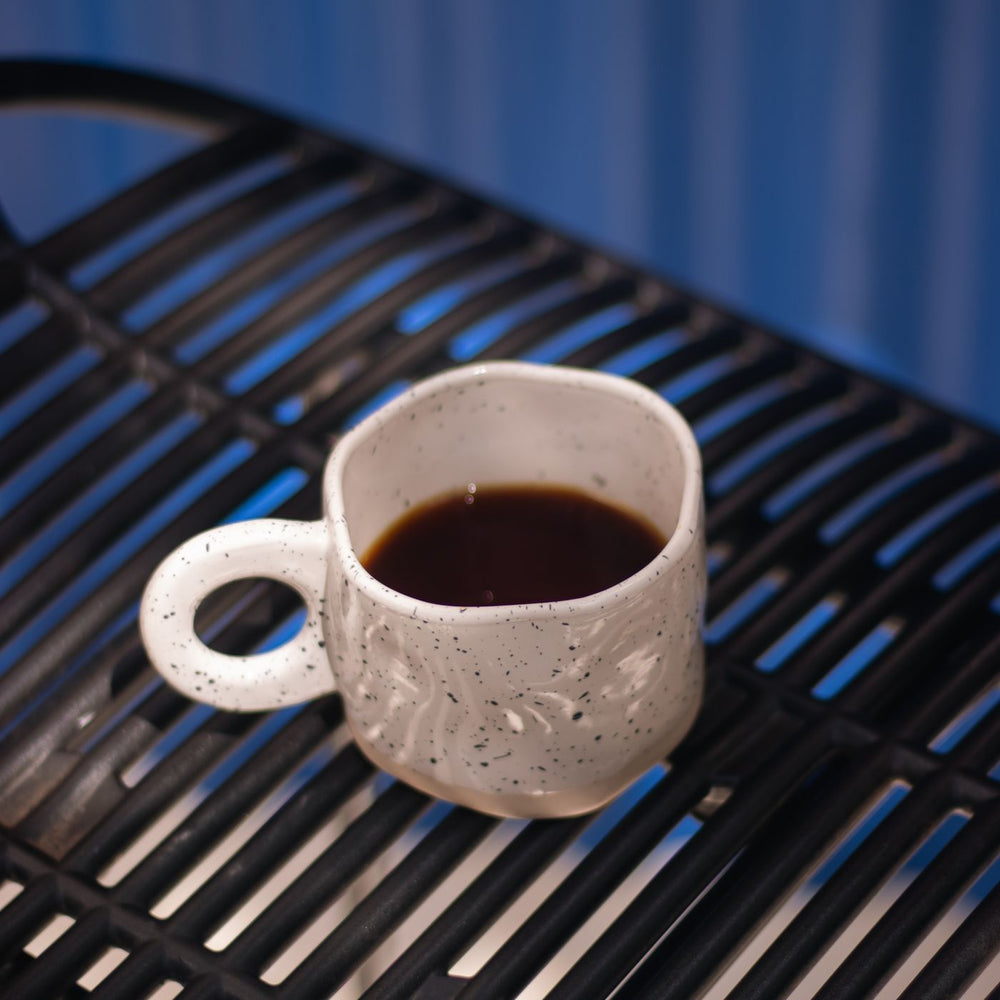 A ceramic coffee mug photographed on a black metal table against a blue backdrop.
