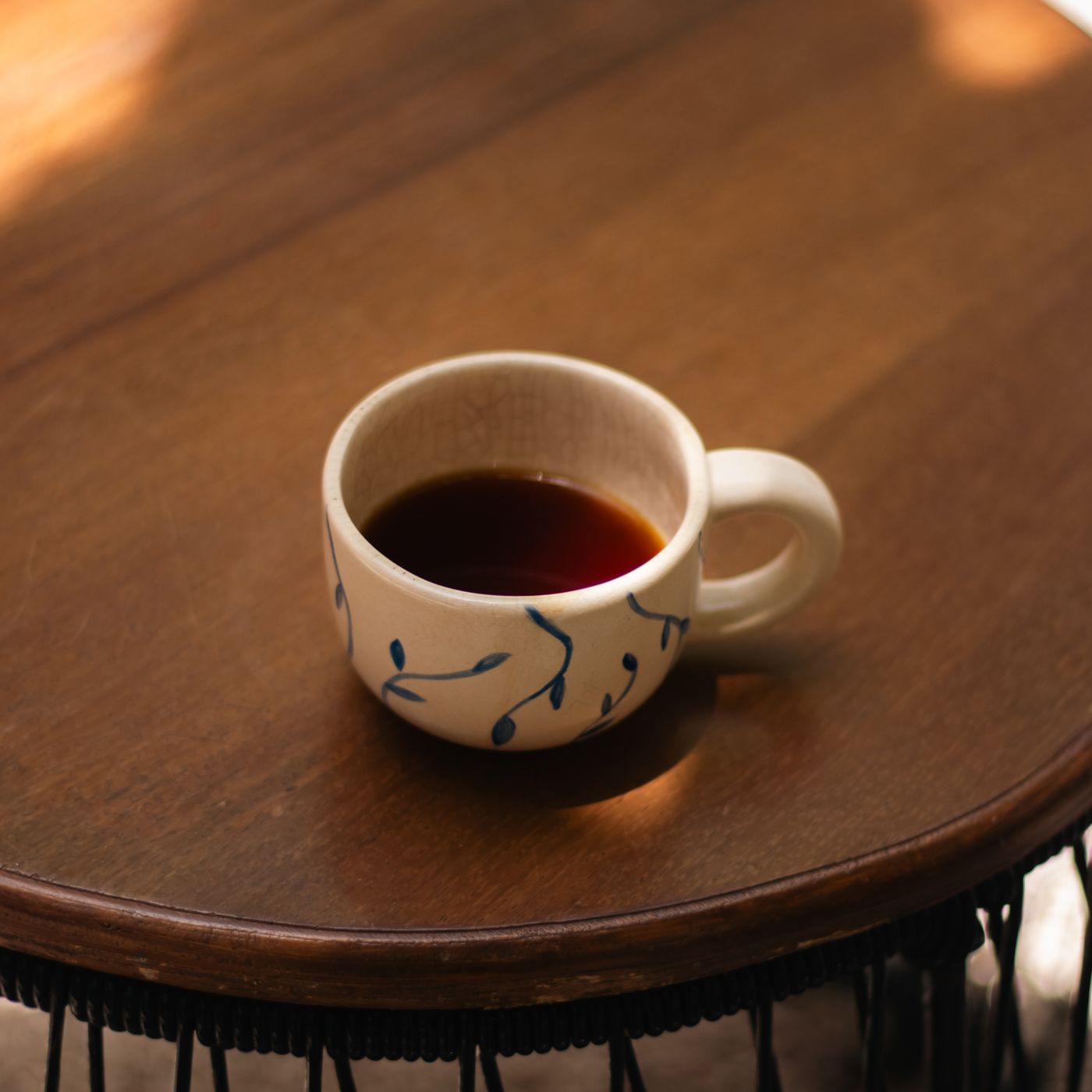 A ceramic coffee cup finished with blue accents, photographed on a wooden table in warm sunlight.