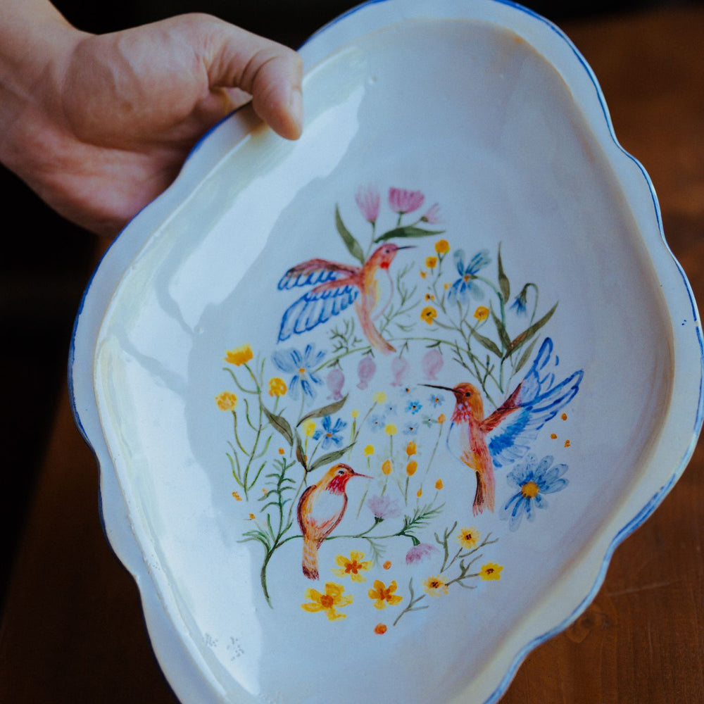 A hand painted ceramic dish featuring birds among flowers.