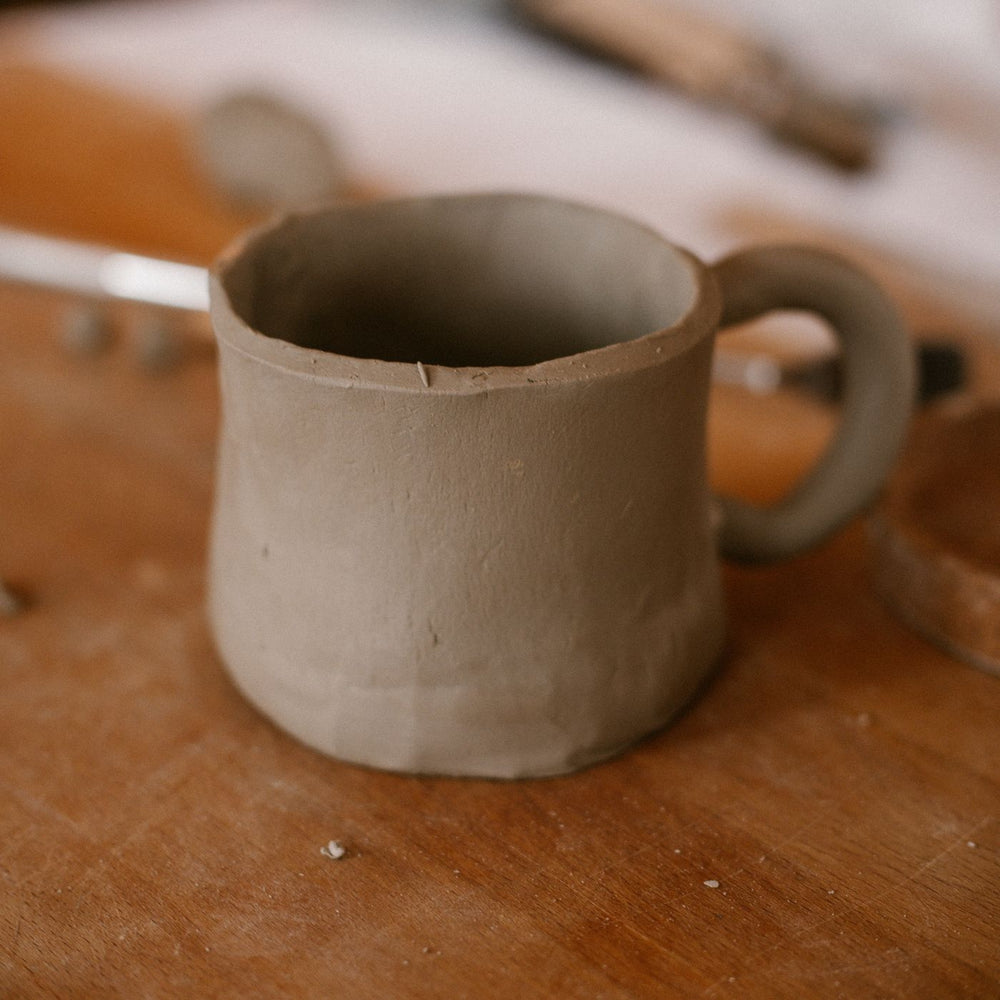A rustic handmade clay mug photographed on a wooden table in our pottery studio.