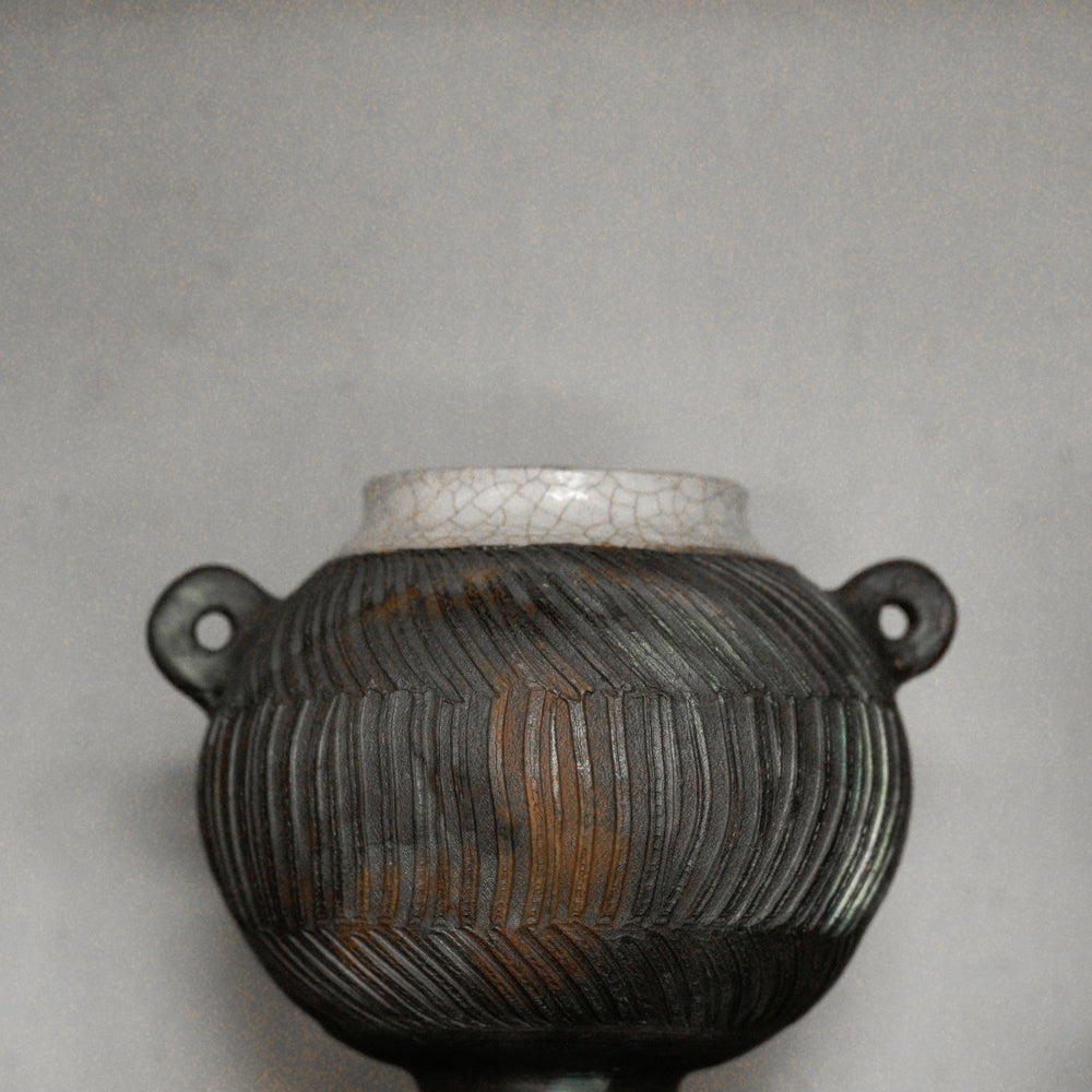 An antique-looking ceramic vessel with a heavily worked surface and muted, faded colouring.