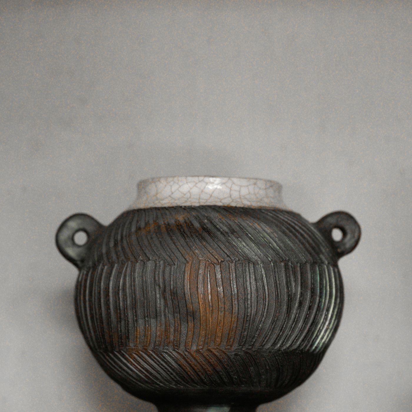 An antique-looking ceramic vessel with a heavily worked surface and muted, faded colouring.