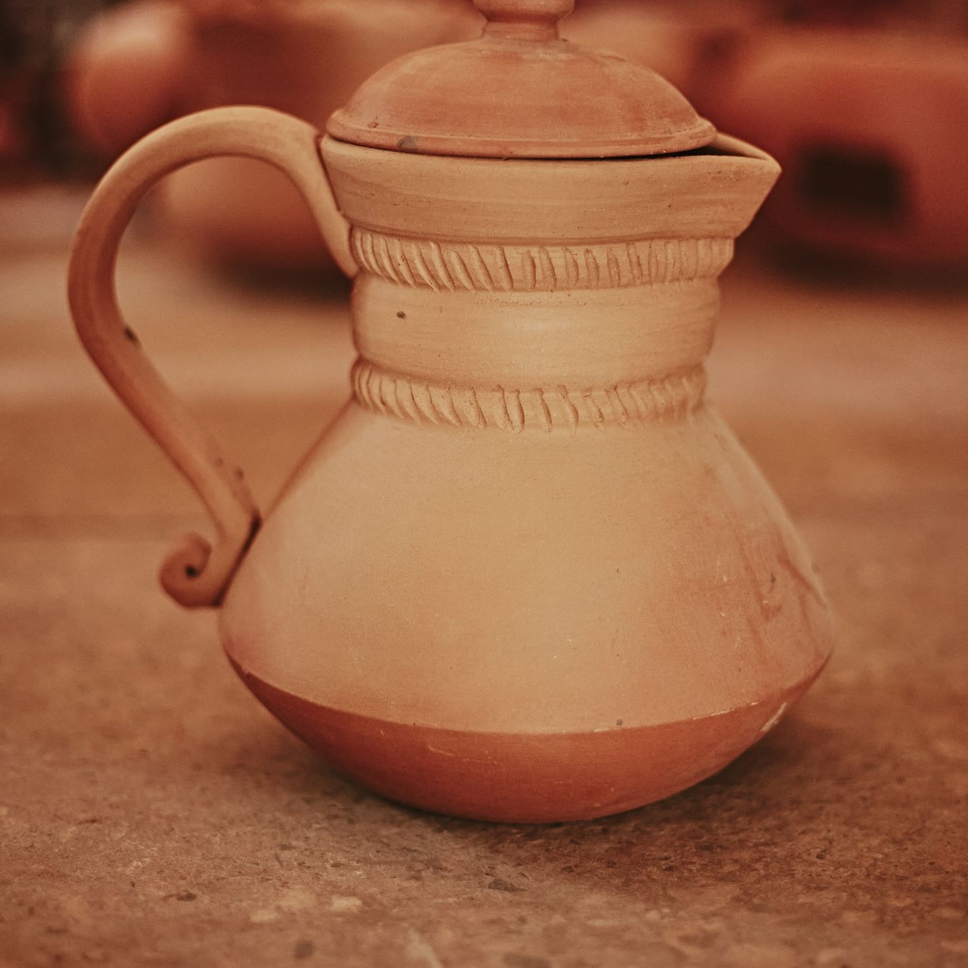 A vintage-style clay teapot worked with an intricate design, photographed standing on a textured stone surface.