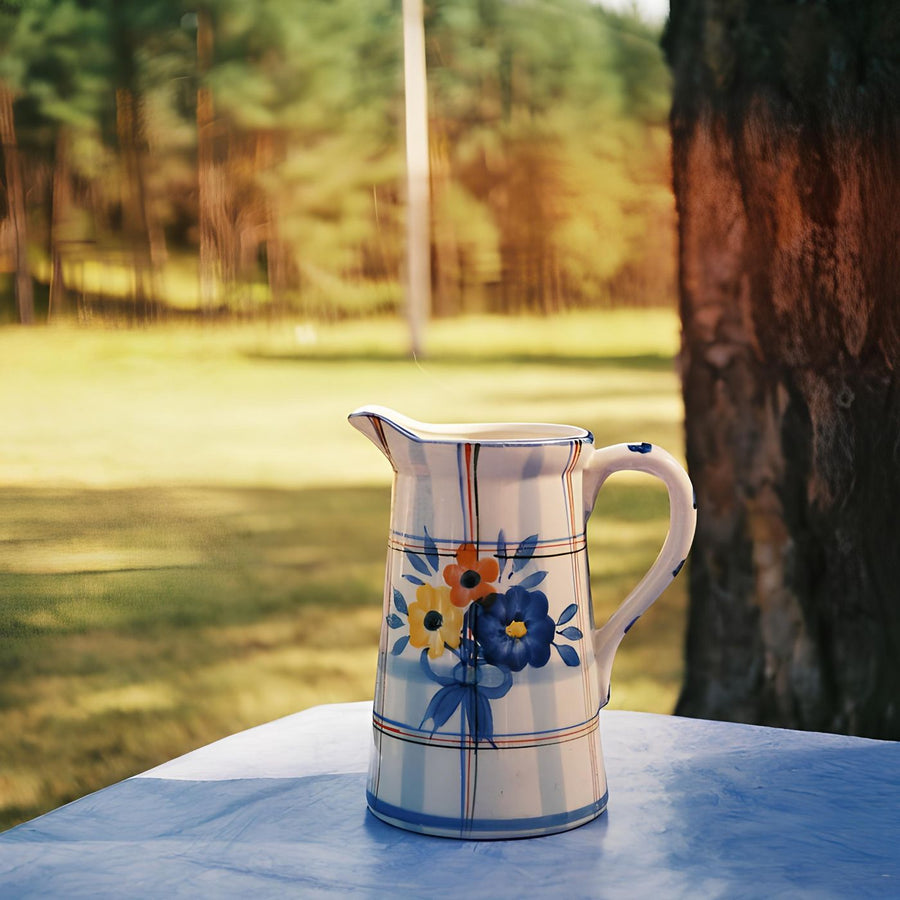 A vibrant ceramic jug decorated with painted flowers, photographed on a table outdoors.