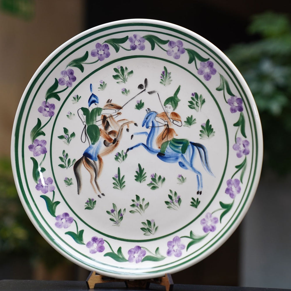 An ornate ceramic plate hand painted with colourful horsemen and floral motifs.