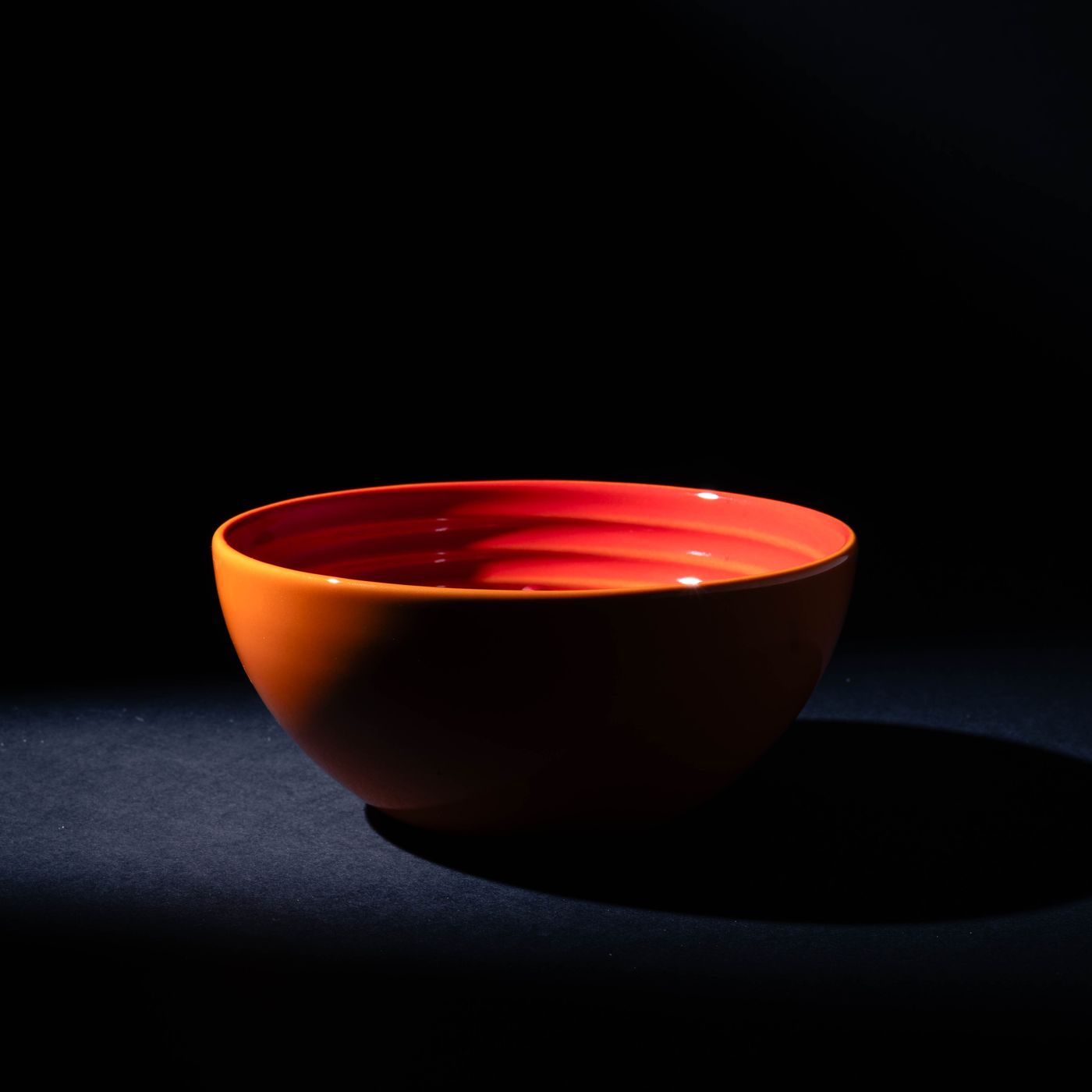A vibrant orange red bowl, shot as a striking minimalist study against a dark background.