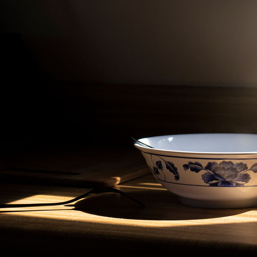 A ceramic bowl carrying a blue floral design, photographed under warm dramatic light on a wooden table.