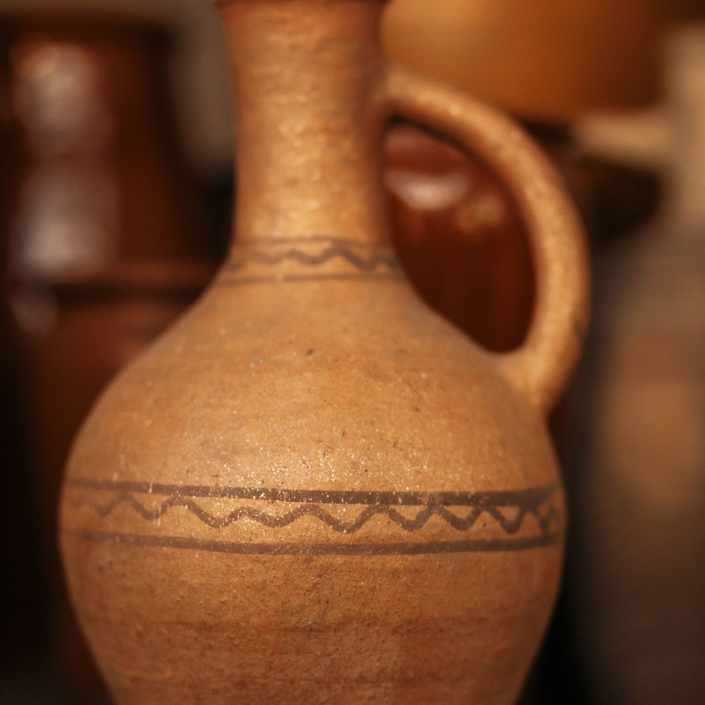 A handcrafted clay jug with intricate patterning, photographed close up on a shelf.