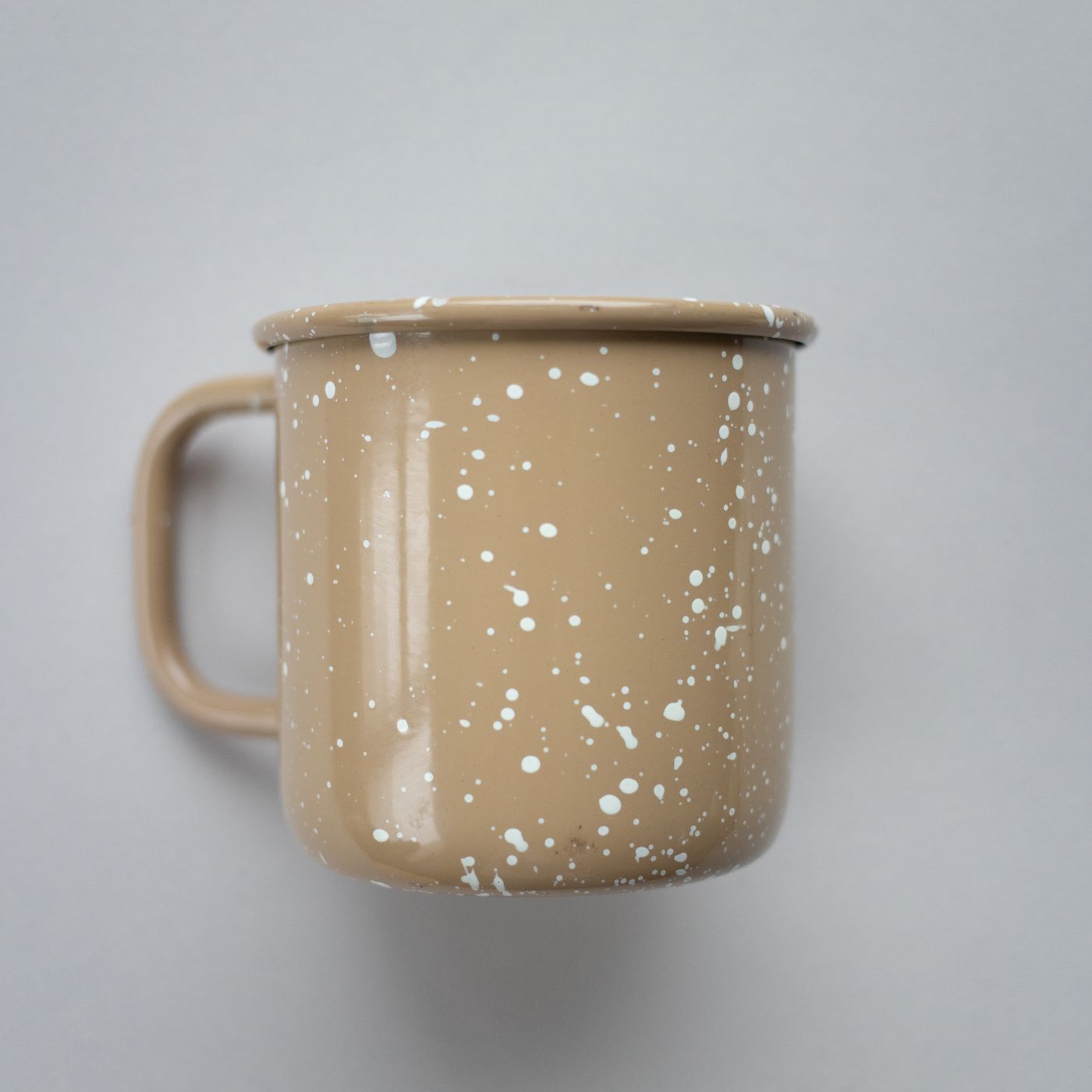 A minimalist beige speckled coffee mug shown against a neutral grey background.