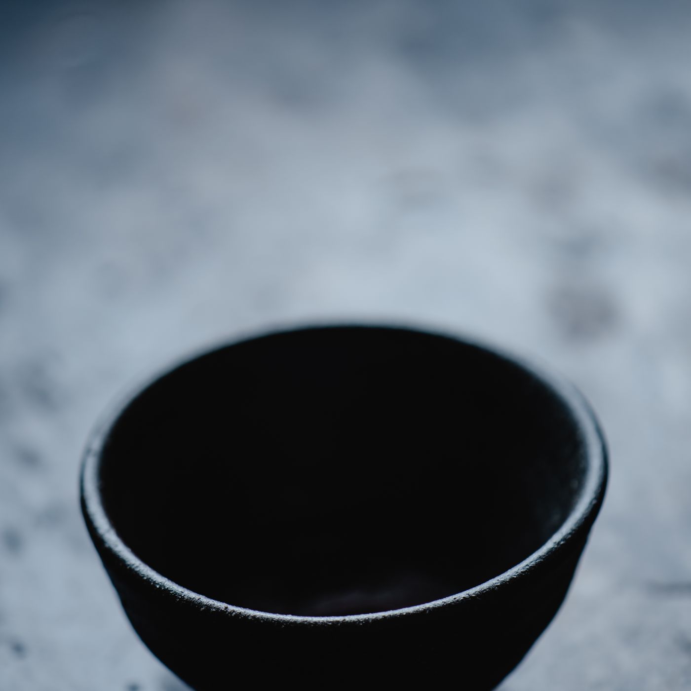 An empty black ceramic bowl with a plain minimal profile, shown on a dark textured surface.