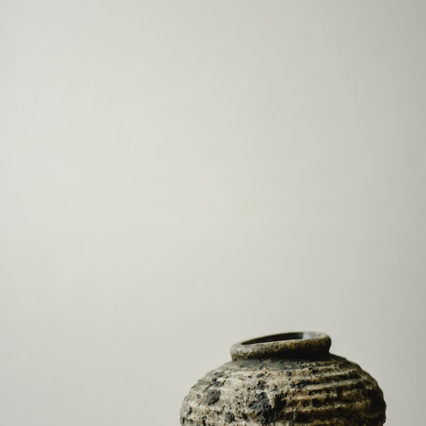 A vintage looking ceramic jar, photographed on a concrete block against a neutral background.