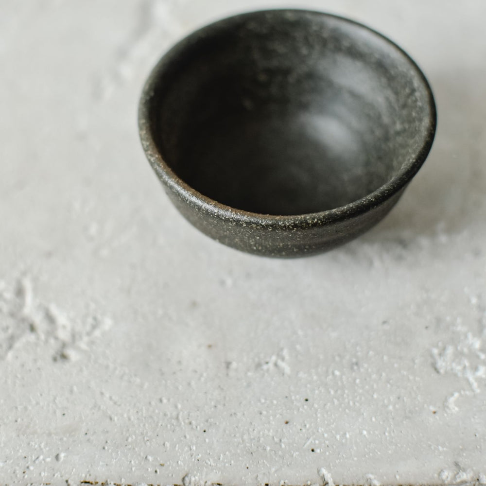 A minimalist stoneware bowl photographed close up on a textured concrete surface.