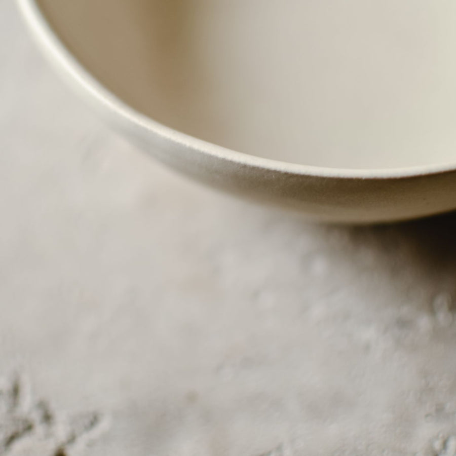 A simple beige ceramic bowl photographed on a textured stone surface.