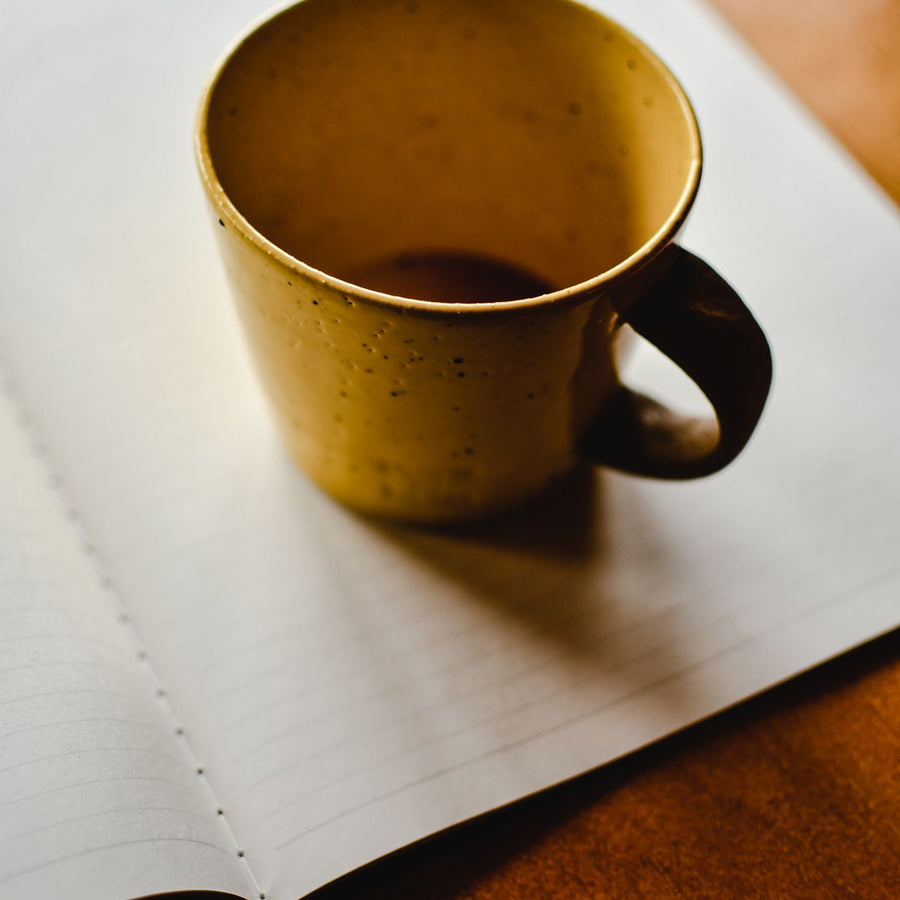 A small brown ceramic cup, shown empty and resting on an open notebook on a wooden desk.