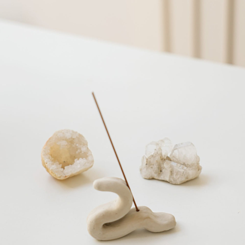 An elegant ceramic incense holder, photographed on a minimalist table with crystals set beside it.
