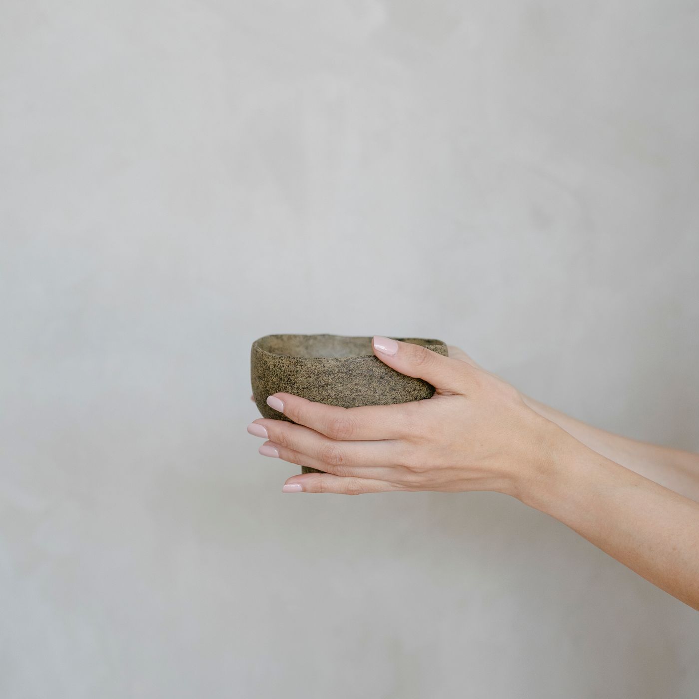 A rustic handmade stoneware bowl, photographed held in two hands against a grey background.