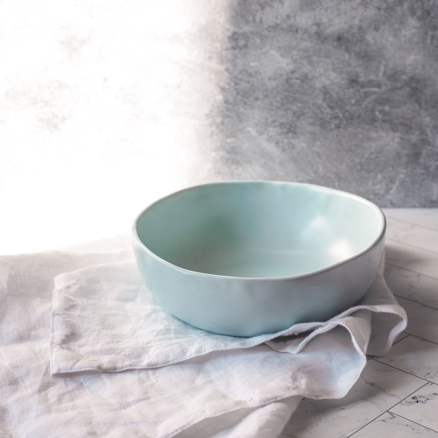 A light blue ceramic bowl, photographed arranged on a marble countertop.