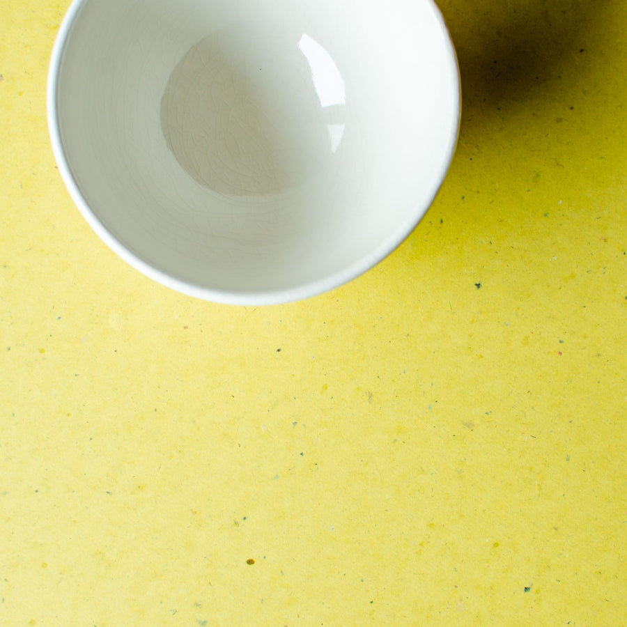 A plain empty white bowl, photographed on a bright yellow surface.